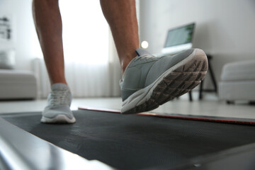 Sporty man training on walking treadmill at home, closeup © New Africa
