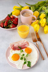 Festive breakfast with fried eggs, bleak, coffee, strawberries, orange juice and a bouquet of tulips on the table. Romantic breakfast serving.