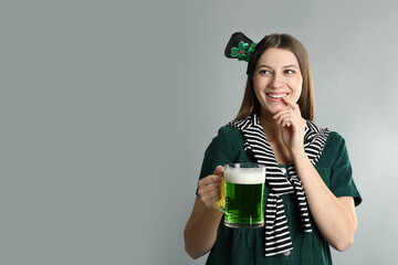Happy woman in St Patrick's Day outfit with beer on light grey background, space for text