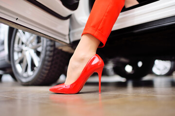 close-up of a woman's leg in a red suit and red shoes against the background of a car. The concept of a woman driving a car.