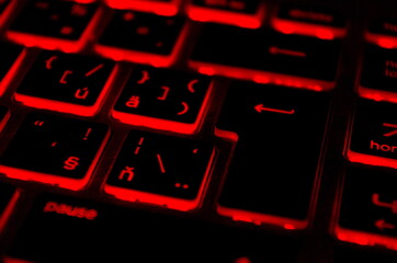 Modern red iluminated backlit keyboard. Red backlight, backlit on laptop or keyborad computer of gaming in the dark. Cyber Attack, hacking and Internet security concept. 