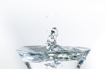 Close-up of water drop falling into a glass on white background