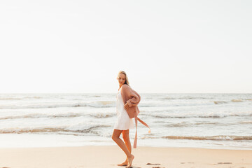 Fototapeta na wymiar Young slim woman walk alone on the beach or ocean at summer sunset. Female dressed in a warm sweater.