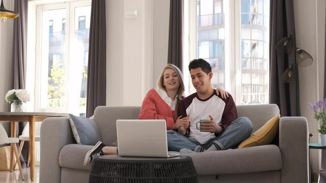 Young couple on a video call with their laptop while sitting on a couch together at home.