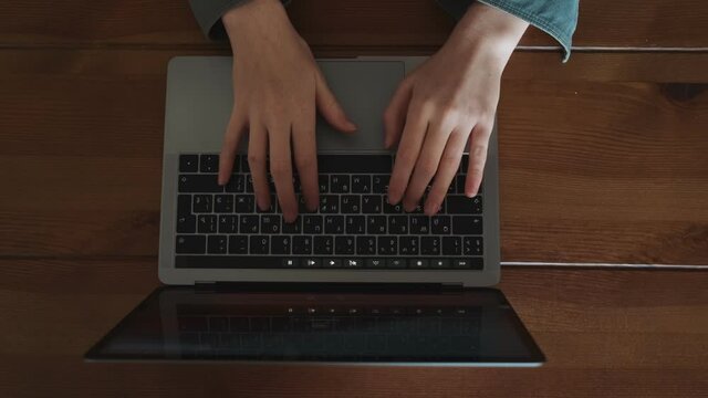 A top view of a young woman is typing on the keyboard on her laptop computer sitting at the table in the apartments