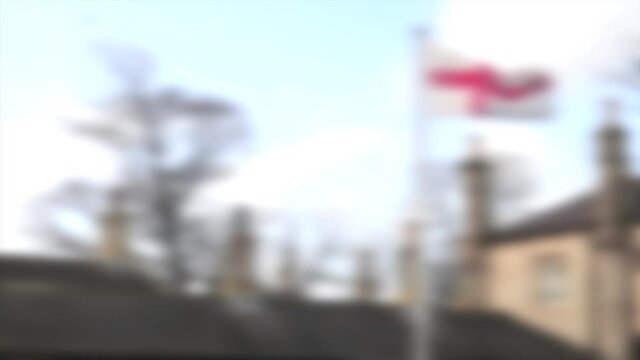 Abstract blurred St Georges Flag for England flying on a flagpole over the top of rooftops with chimney stacks