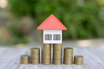 An orange house placed on a pile of coins Home plan ideas, saving money, investing in real estate for saving or investing for a house and paying taxes.