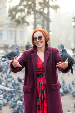 Elderly woman with red hair feeding pigeons in the park