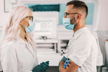 Two dedicated lab assistants standing in laboratory and talking about new cure for corona virus.