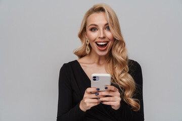 Excited blonde girl in luxury earrings using mobile phone