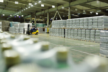 Yellow loader on the background of a huge industrial food warehouse with plastic PET bottles with...