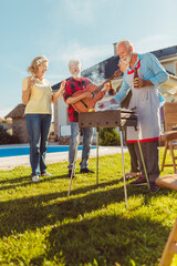 Senior people playing the guitar and singing at backyard barbecue party