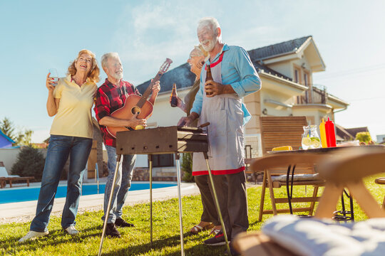 Elderly friends playing the guitar and singing at backyard barbecue party