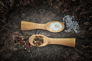 Wooden  spoons filled with salt crystals and black peppercorns. On old wooden background. Vintage effect. 