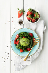 Salad with strawberries, avocados, spinach on a white wooden background top view flat lay
