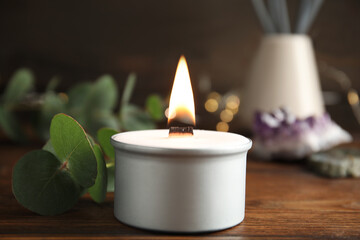Burning candle and eucalyptus on wooden table, closeup