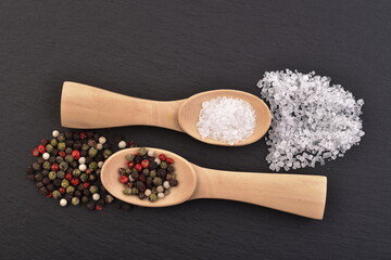 Colored pepper ans salt crystal on a wooden spoons on a black stone background.
