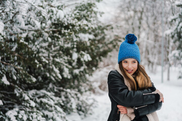 Happy beautiful girl in knit hat smiling while walking in winter park