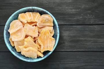 Delicious dried jackfruit slices in bowl on black wooden table, top view. Space for text