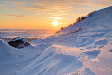 Winter arctic landscape. Morning view from the snow-covered mountainside to the sunrise over the frozen sea and tundra. Cold windy and frosty weather. Beautiful sunrise. Chukotka, Siberia, Russia. © Andrei Stepanov