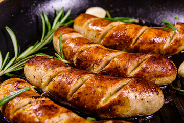 Roasted sausages with rosemary twigs and garlic in a cast iron grill pan