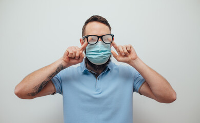 Handsome man with beard wiping blurred foggy misted glasses caused by wearing medical mask on light background. Covid-19