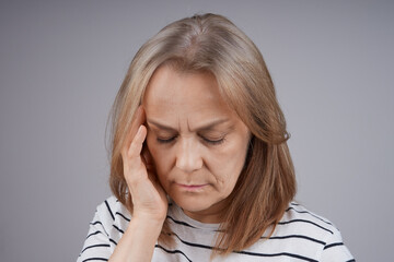 Middle-aged woman, holding her head, suffering from pain. Isolate on gray background