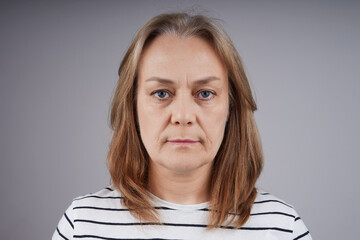 Portrait of a nice middle-aged woman in a striped shirt looking at the camera. studio shot on gray background