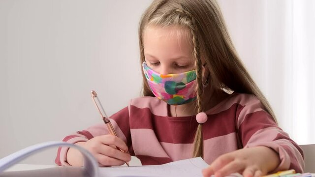 Little girl child wear face protective mask studying at school in classroom and doing homework lesson after quarantine covid-19. Education pandemic, new normal.