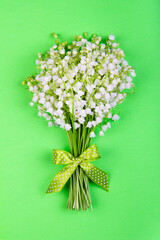 bouquet of lily of the valley flowers with a green bow on a green background top view close up