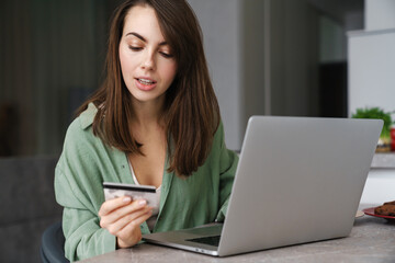 Focused nice woman using credit card while working with laptop