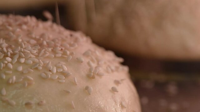 Baker sprinkles sesame on the raw dough. Close-up. The process of making round bread