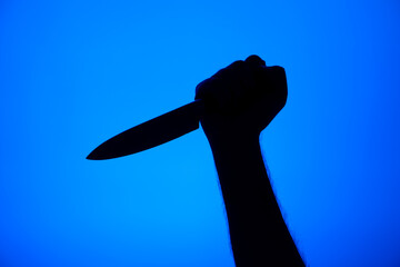 Knife stabbing gesture silhouette black on blue background studio shot unrecognizable