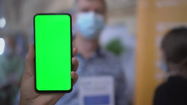 Back view of brunette holding chroma key green screen smartphone watching content. Gadgets and contemporary people concept.