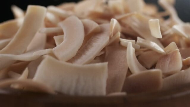 Coconut chips are falling down to wooden bowl close-up, slow motion