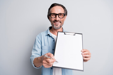 Portrait of cheerful guy hands hold pen clipboard show you where to sign isolated on grey color background