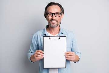 Photo of handsome man happy positive smile hold clipboard show document isolated over grey color...