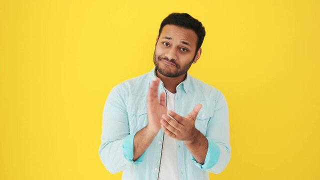 A pleased indian man is looking to the camera and clapping his hands standing isolated over yellow background in studio