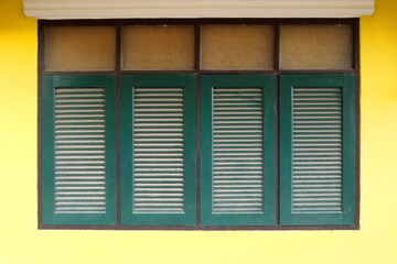 Row of retro dark green windows in rectangle shape and bright yellow wall of house in Thailand.