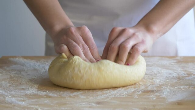 Woman kneading pastry dough on floured baking board