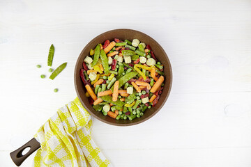 Frozen vegetables in a frying pan on a white wooden background. Top view.