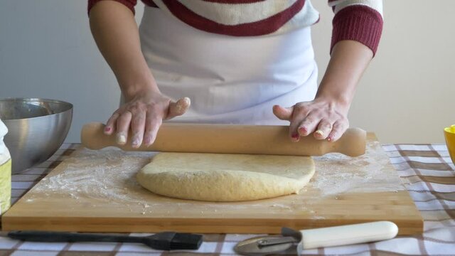 Woman flattening pastry dough with rolling pin on baking board