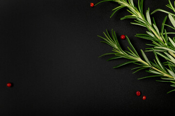 Sprigs of fresh rosemary and pink pepper grains of Schinus terebinthifolius on dark background. Workpiece or blank for a culinary-themed design. Top view