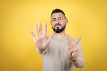 Handsome man with beard wearing sweater over yellow background showing and pointing up with fingers...