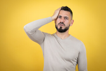 Handsome man with beard wearing sweater over yellow background putting one hand on her head smiling...
