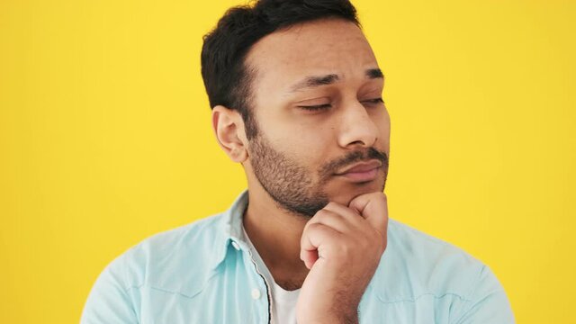 A close-up view of a serious indian man is thinking about something standing isolated over yellow background in the studio