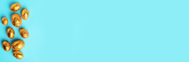Chocolate eggs wrapped in golden foil on light blue background, flat lay with space for text. Banner design