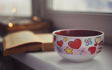 Closeup huge cup of coffee with vintage books on windowsill. Vintage light, blurred and bokeh background. Cosiness, warm and reading concept