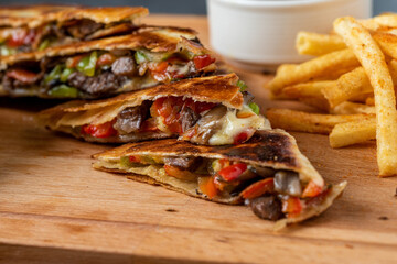 Mexican quesadilla with meat, cheese and peppers on wooden table.