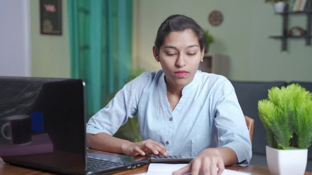Young Indian business woman calculating expenditure by looking into the bills from laptop and paper at home.